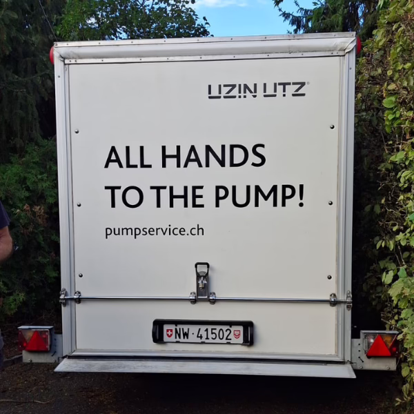 The back of a white service vehicle shows the words ALL HANDS TO THE PUMP! along with a web address and license plate, framed by greenery on both sides.