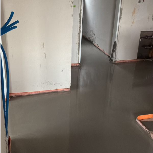 A freshly poured, smooth concrete floor in a building under construction, with unfinished walls, exposed pipes, and doorways leading to other rooms.