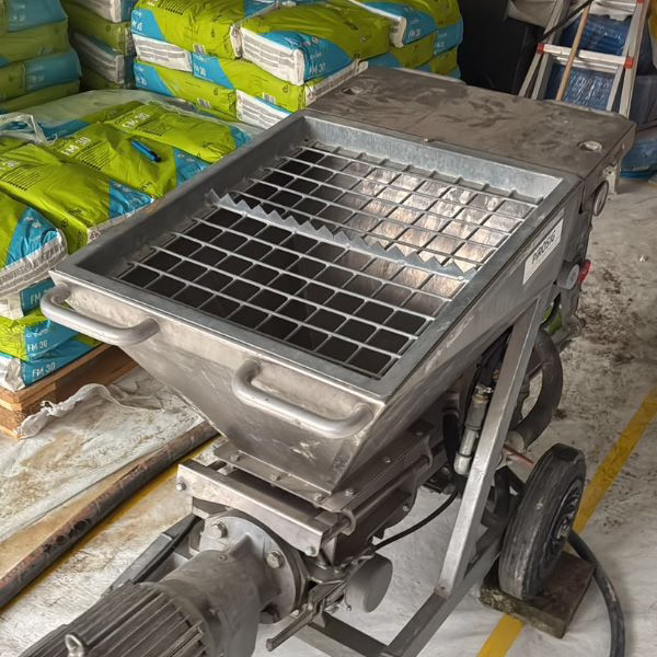 A close-up of an industrial machine with a metal grate on top, surrounded by bags of material and equipment in a workshop or warehouse setting.